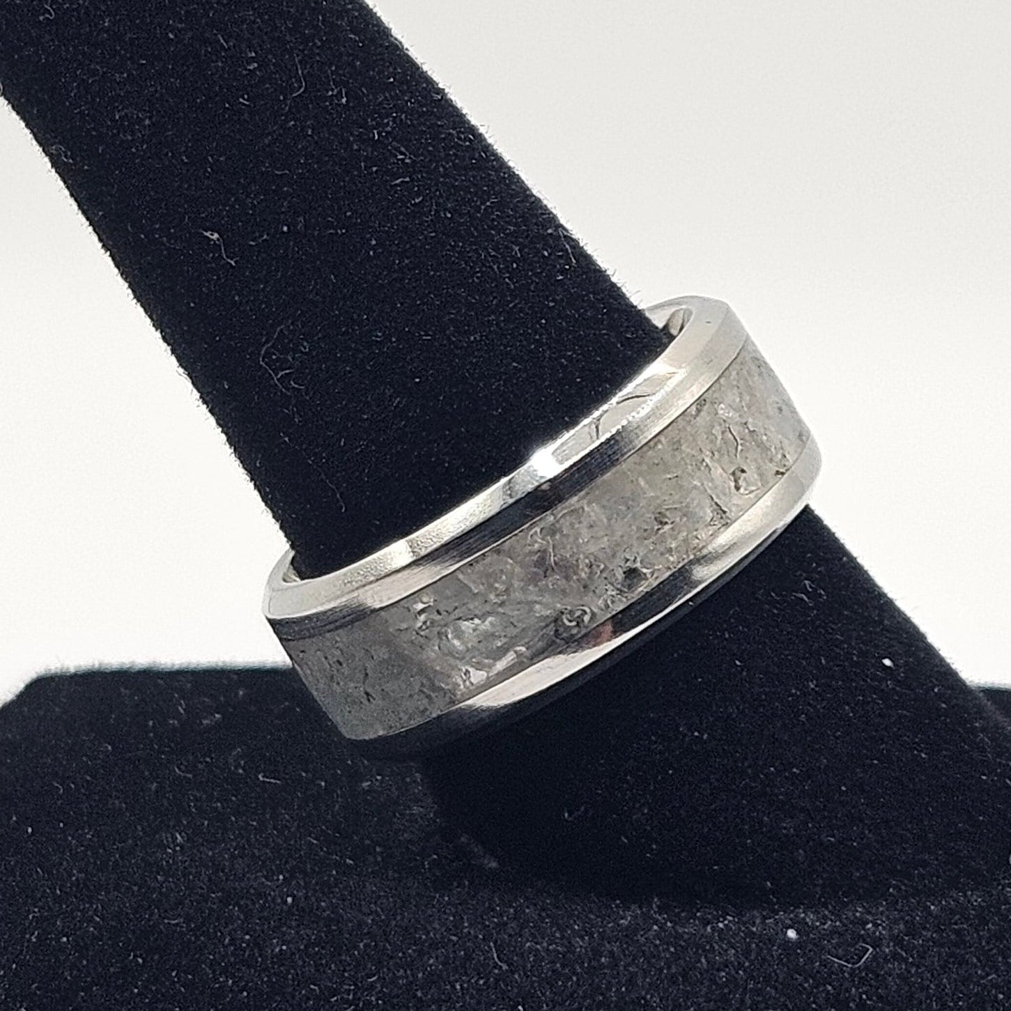 Silver ring on a black cylindrical stand against a white background