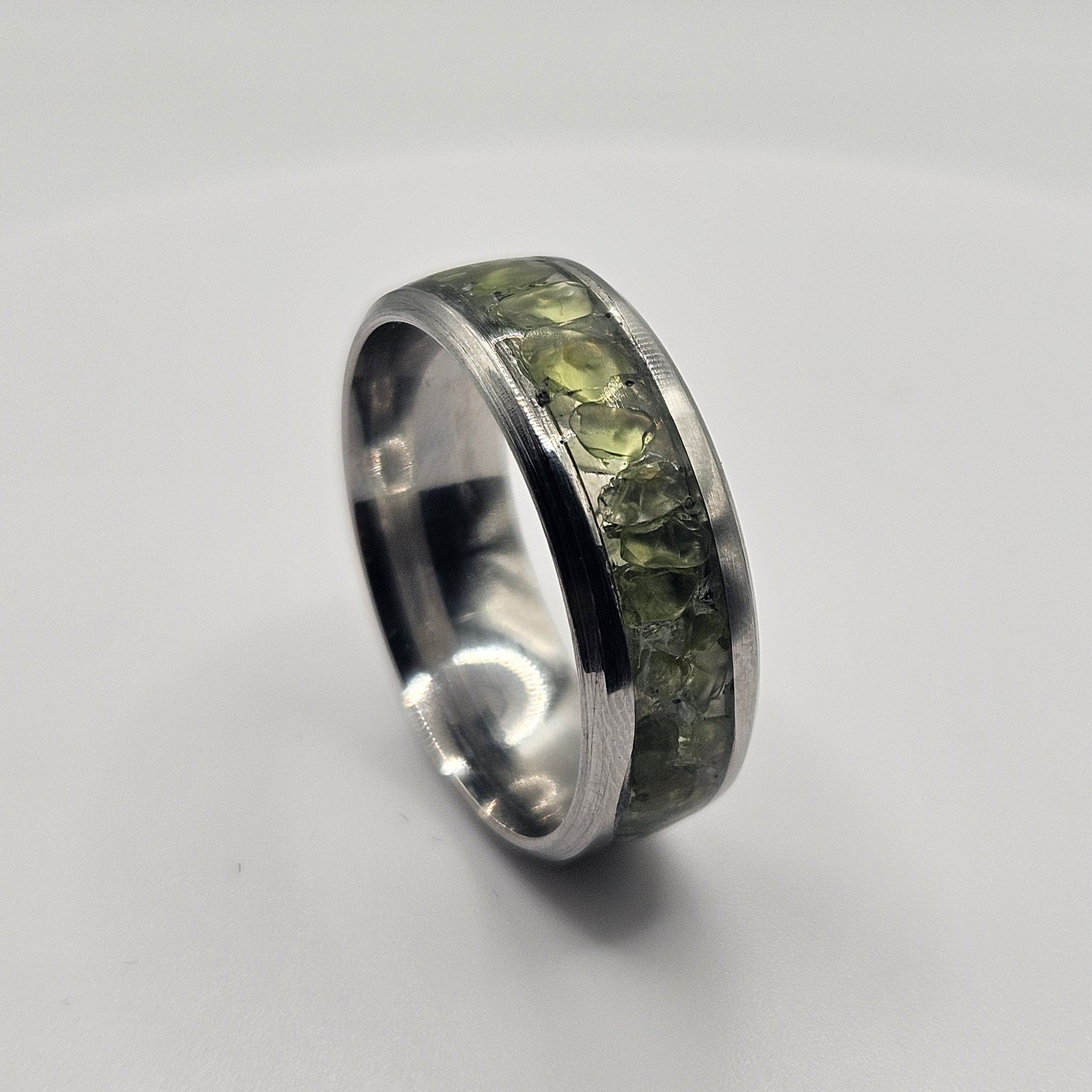 Silver ring with embedded green stones on a light gray background