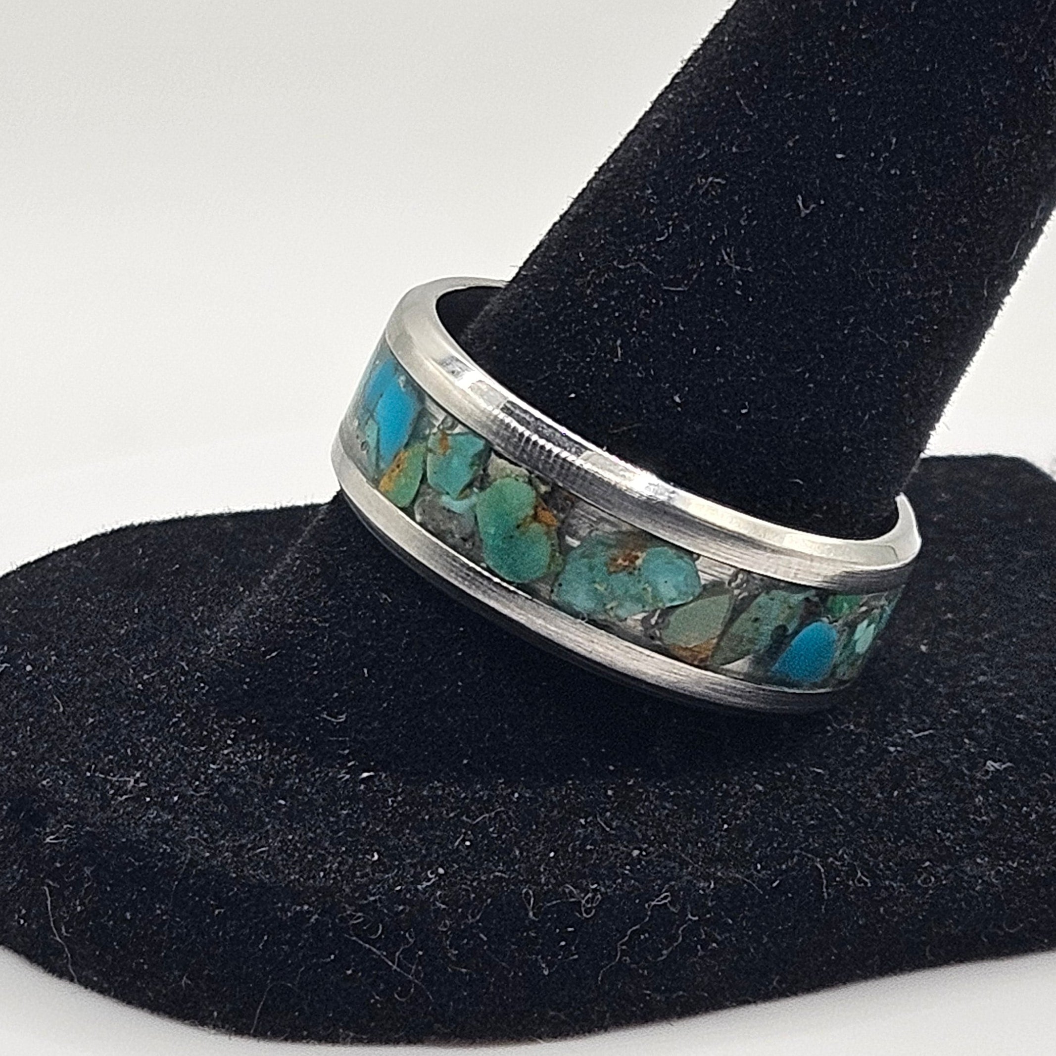 Silver ring with turquoise stones on a black velvet stand against a white background