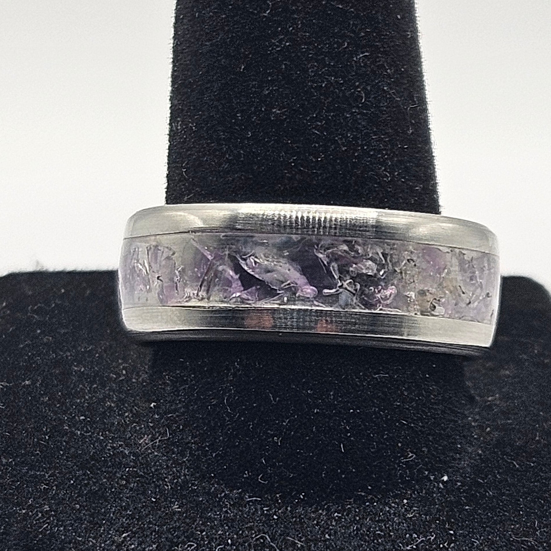 Silver ring with engraved design on a black stand against a white background