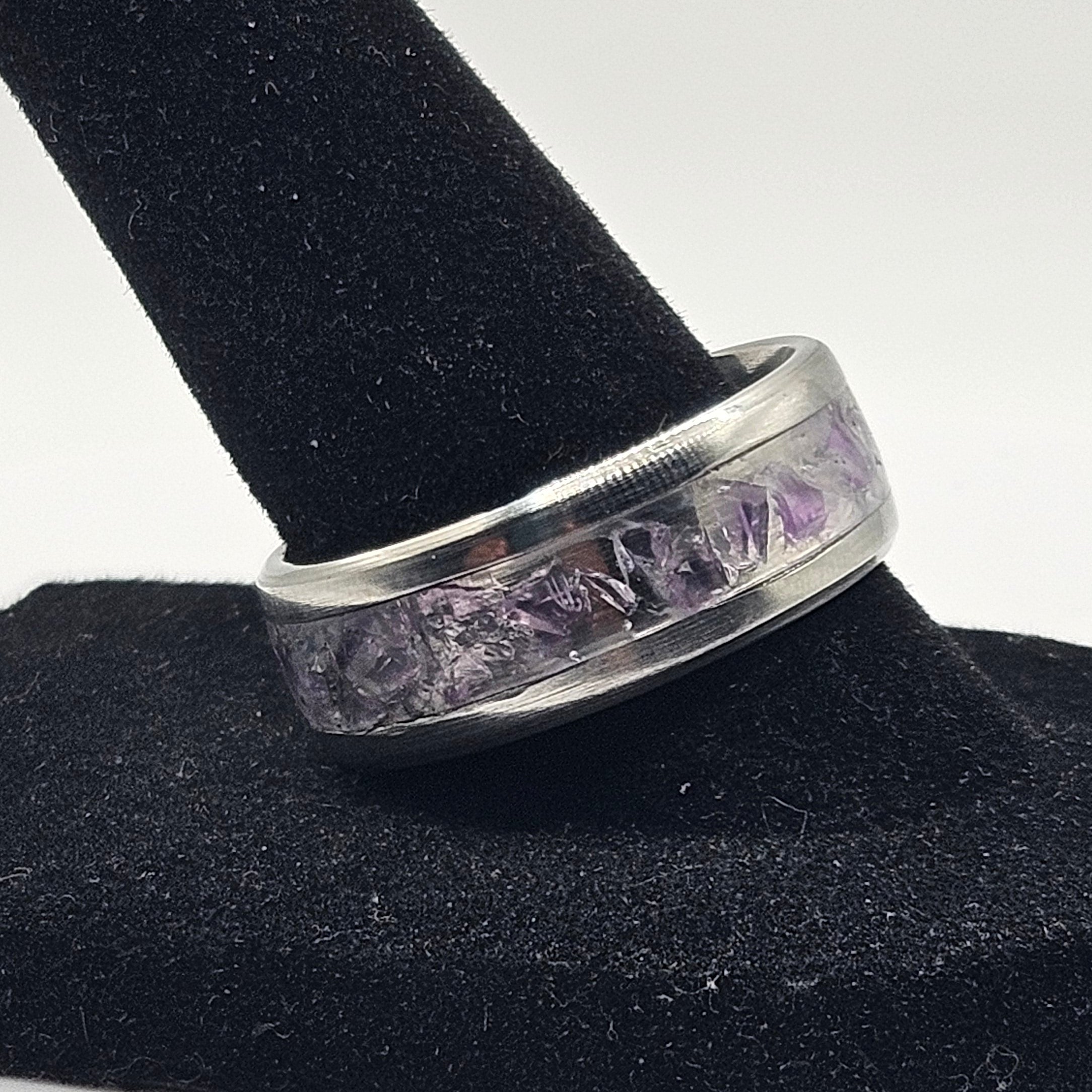 Silver ring with purple inlay on a black stand against a white background