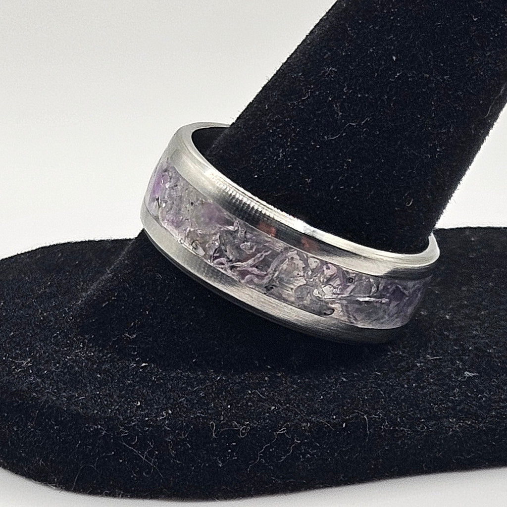 Silver ring with a textured design on a black stand against a white background