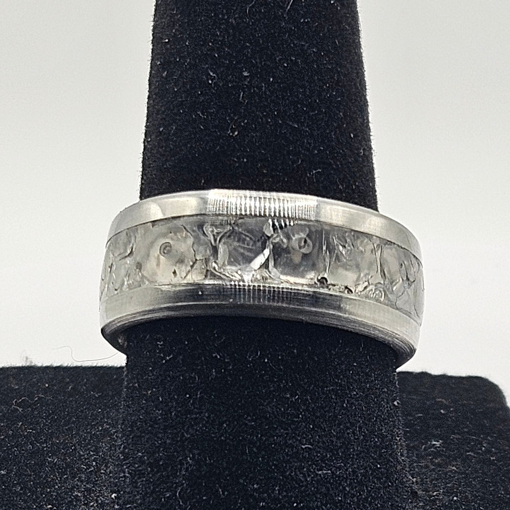 Silver ring with a textured band on a black velvet stand against a white background