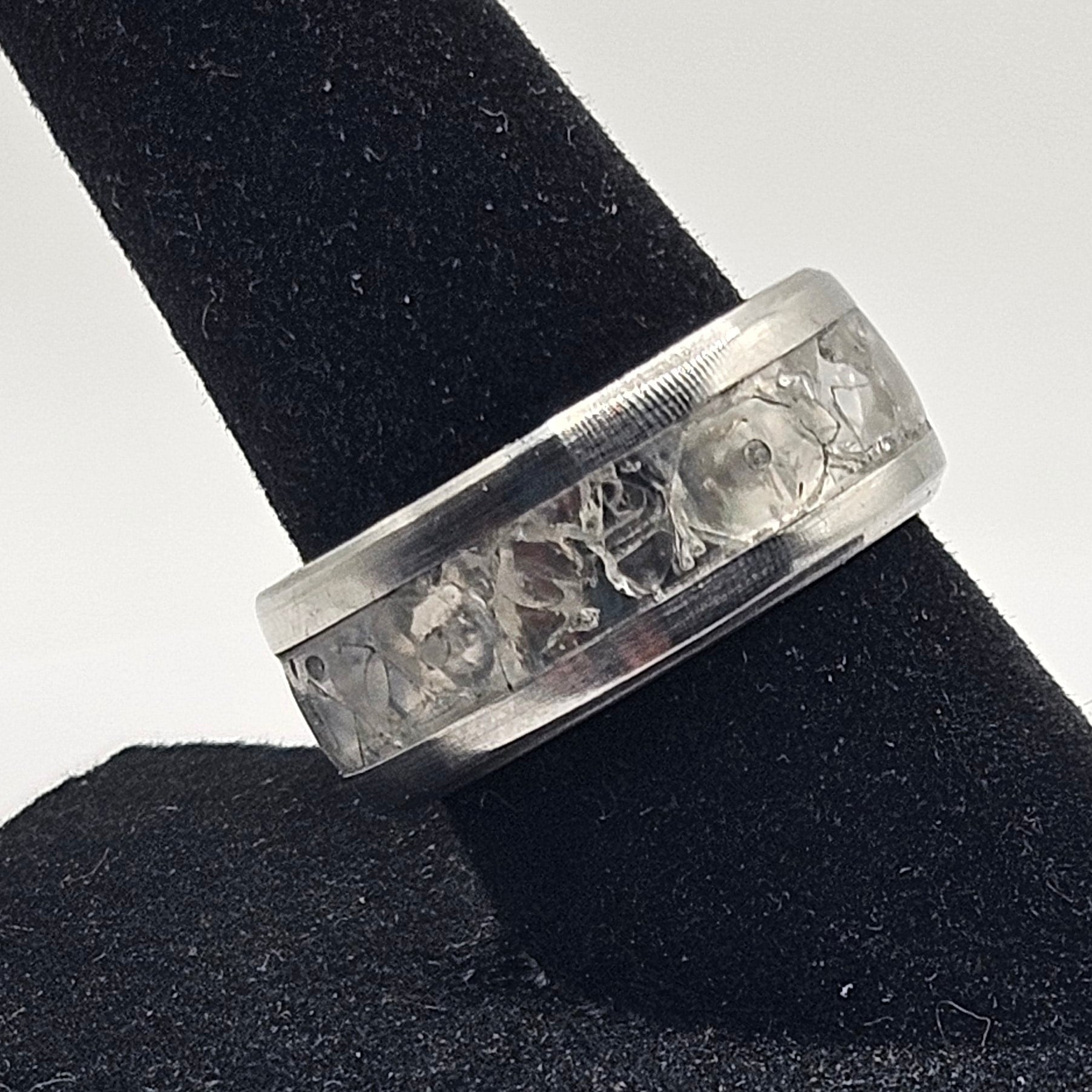 Silver ring with engraved design on a black stand against a white background