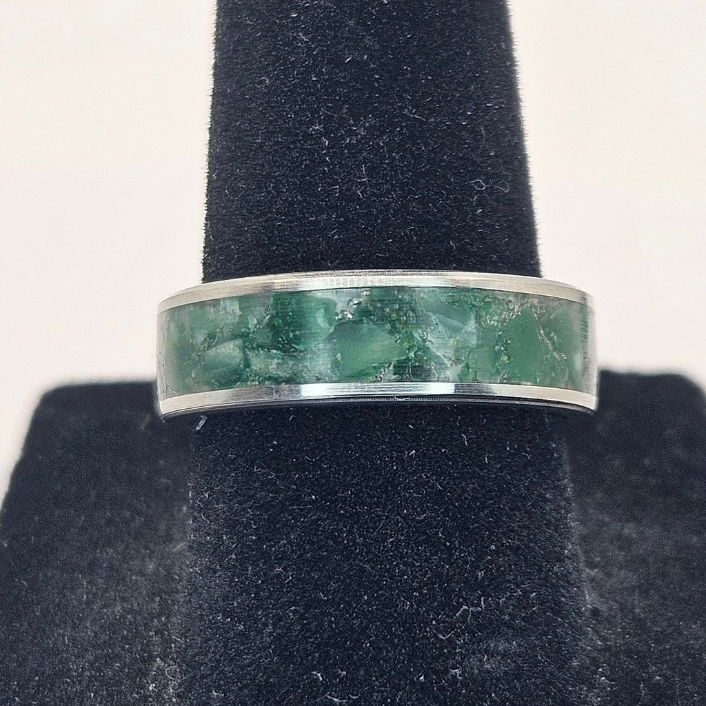 Silver ring with greenstone inlay on a black stand against a white background