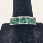 Silver ring with greenstone inlay on a black stand against a white background