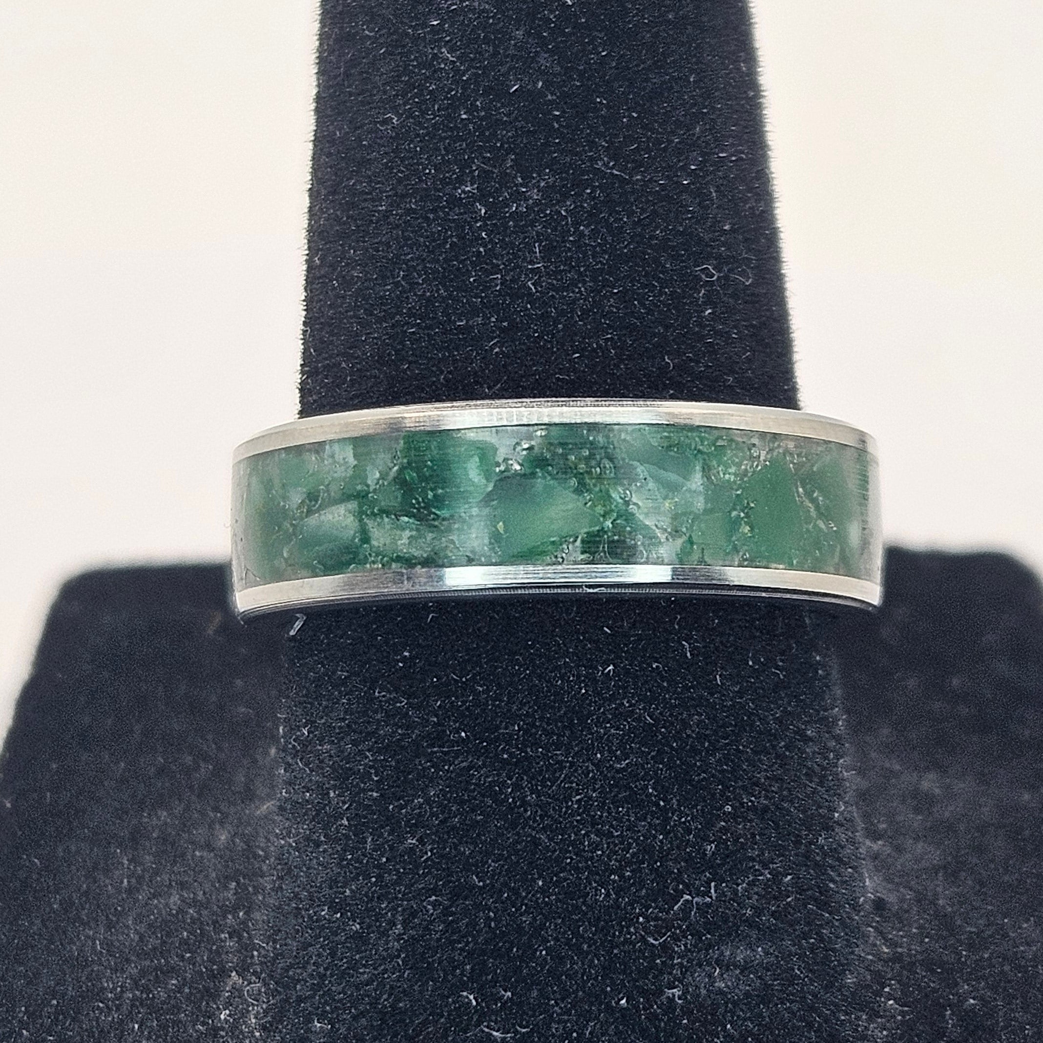 Silver ring with greenstone inlay on a black stand against a white background