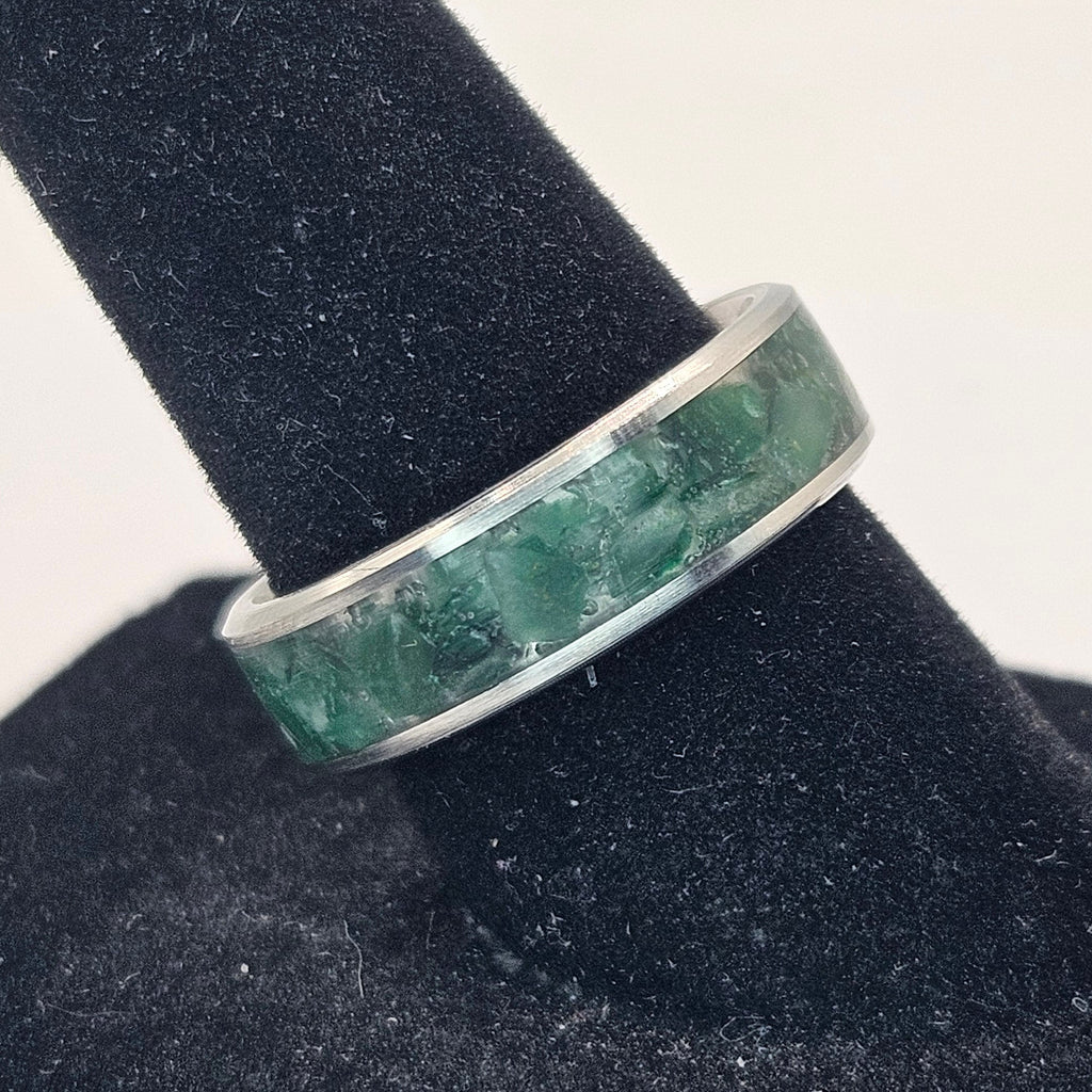 Silver ring with greenstone on a black stand against a white background