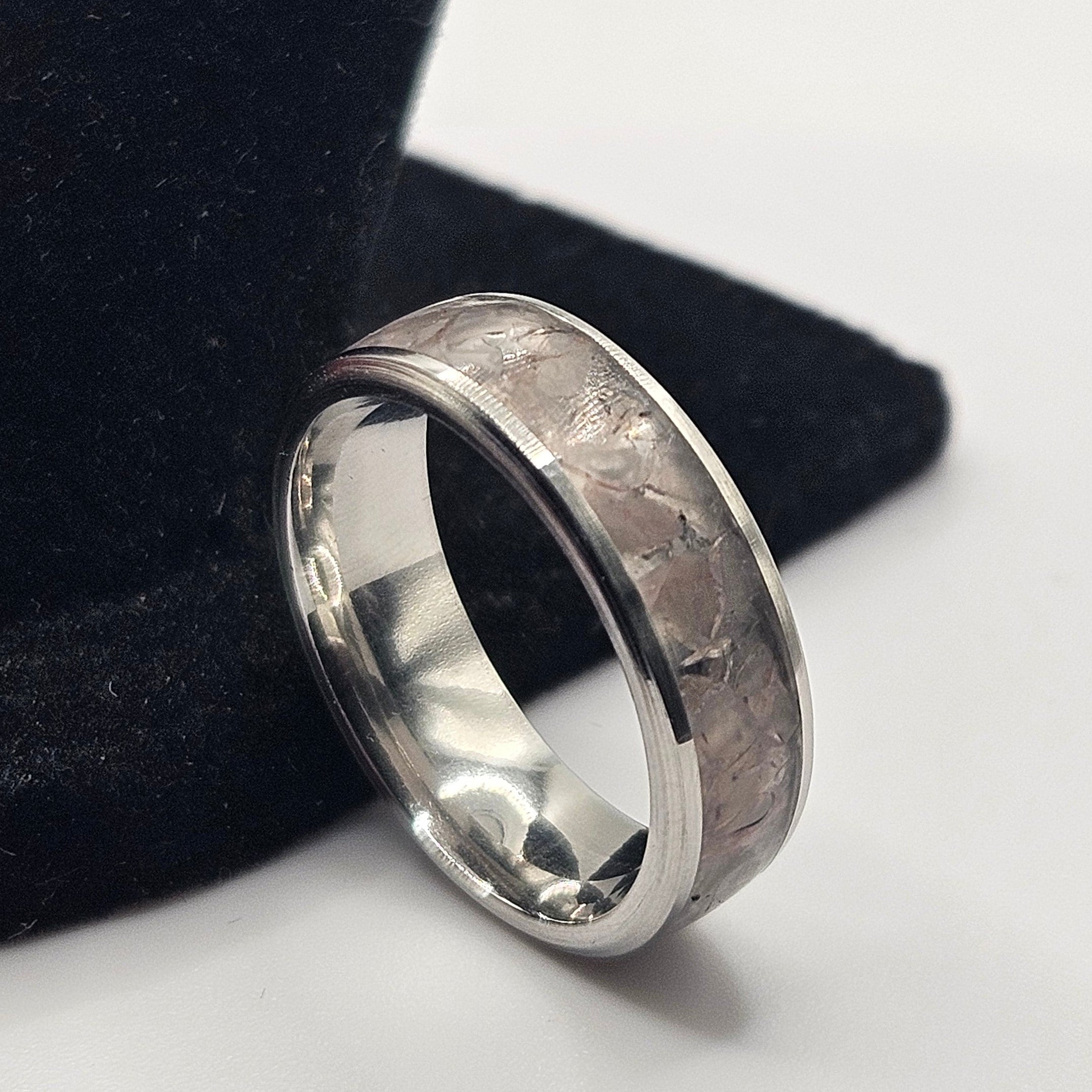 Silver ring with a textured band on a black stand against a light gray background